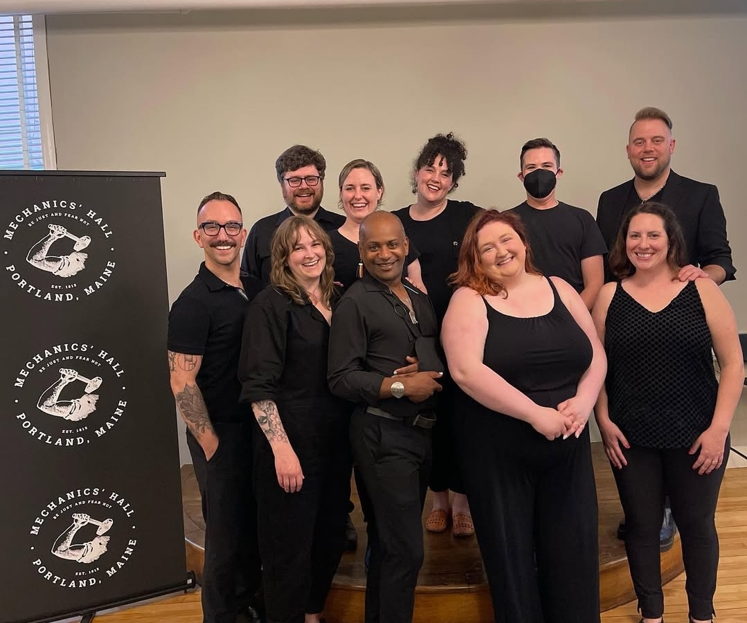 The cast of The Laramie Project stands in two rows, smiling. All are wearing black.